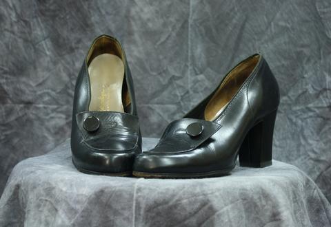 Pumps of black leather with flap over the vamp that has an accent button with stitching representing a button hole