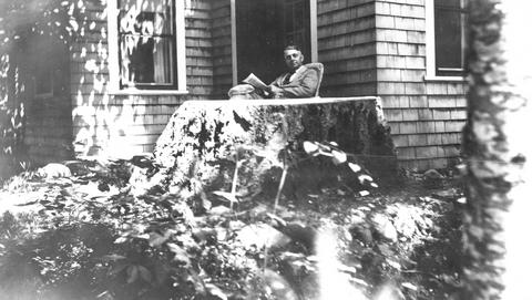 Walter Brown reading on porch at Walker Cottage
